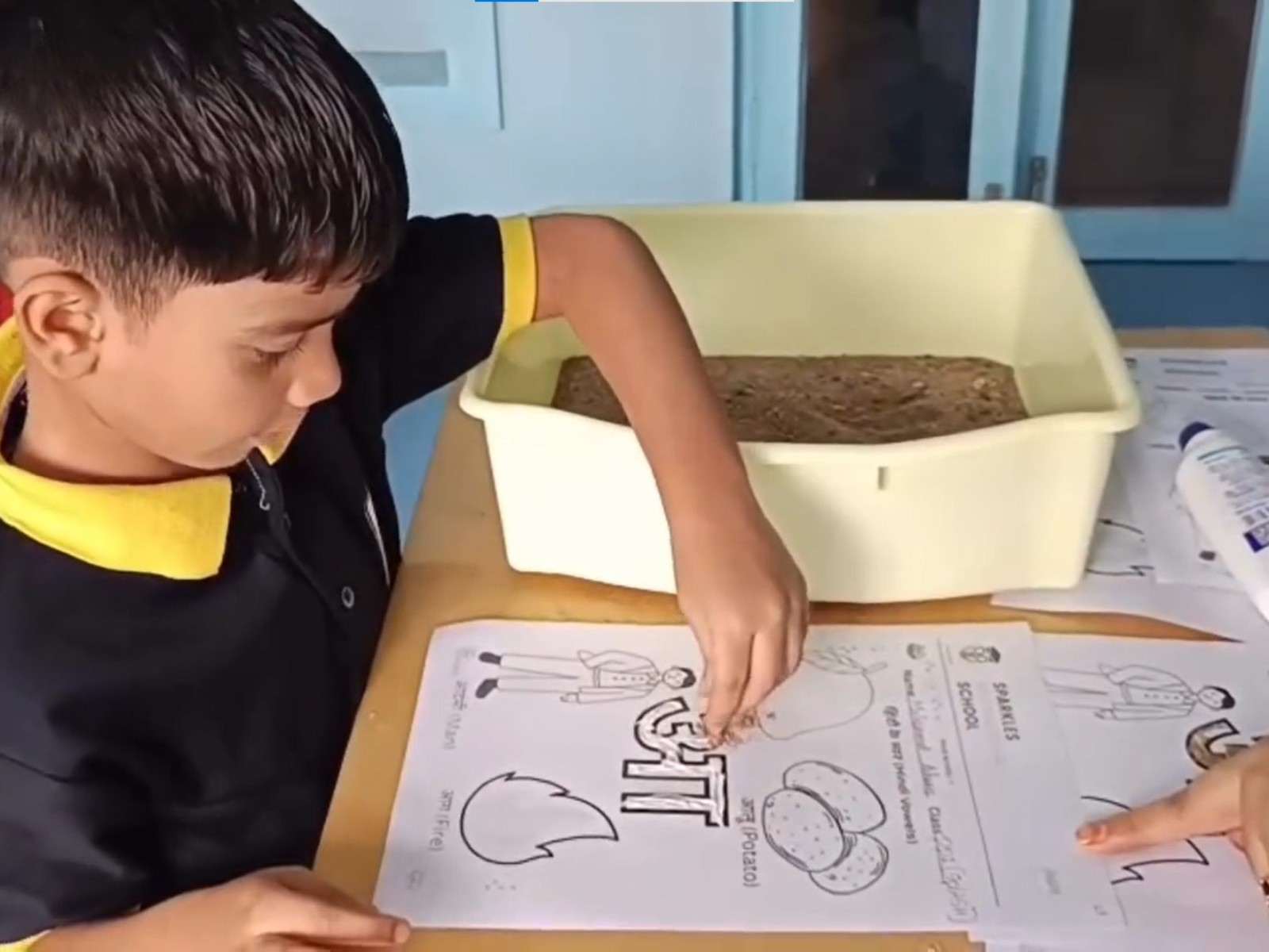 Children tracing Hindi letters with glue and sand at Sparkles International School